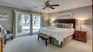 Ein Schlafzimmer mit einem Bett, einer Bank, einem Nachttisch, einem Deckenventilator und Blick ins Freie durch eine Schiebetür.