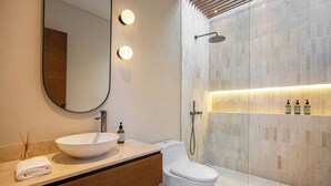 Une salle de bain moderne avec un grand miroir, un lavabo blanc, des toilettes et un espace douche avec un mur carrelé.