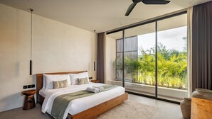 Une chambre moderne avec un grand lit, un ventilateur de plafond et une vue sur la verdure grâce à de grandes fenêtres.