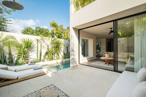 Ein moderner Außenbereich mit Pool, Liegestühlen und einer Glastür, die in ein Wohnzimmer mit Sofa und Couchtisch führt.