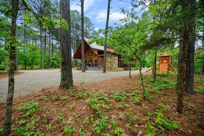Une cabane entourée d’arbres, avec une allée de gravier menant à l’entrée.