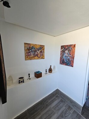 A hallway with two abstract paintings on the walls, a shelf with various decorative items, and a patterned floor. - Studio downtown Rabat terrace (Rabat)