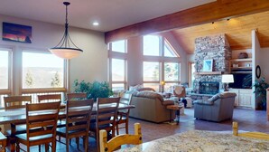 A spacious living area with a stone fireplace, wooden furniture, and large windows. - Views | Hot Tub | Pet Friendly | Sunrise Ridge (Angel Fire)