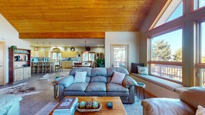 A spacious living area with a large sectional sofa, a coffee table, and a view of the kitchen and dining area. - Views | Hot Tub | Pet Friendly | Sunrise Ridge (Angel Fire)