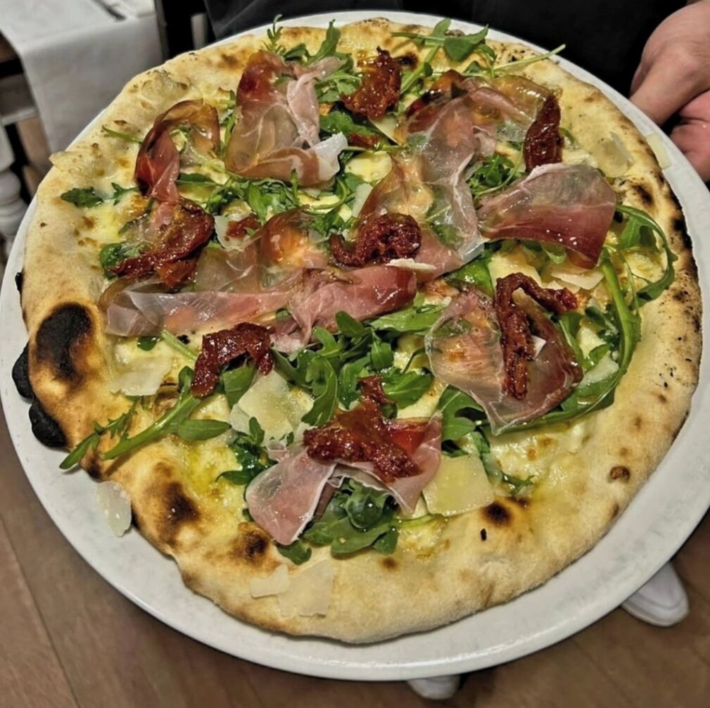 A pizza with arugula and prosciutto on a white plate.