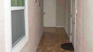 A narrow hallway with a window on the left, a door at the end, and a mat at the entrance. - Unit B Cozy 1 bedroom 1 bath Studio. (Tampa)