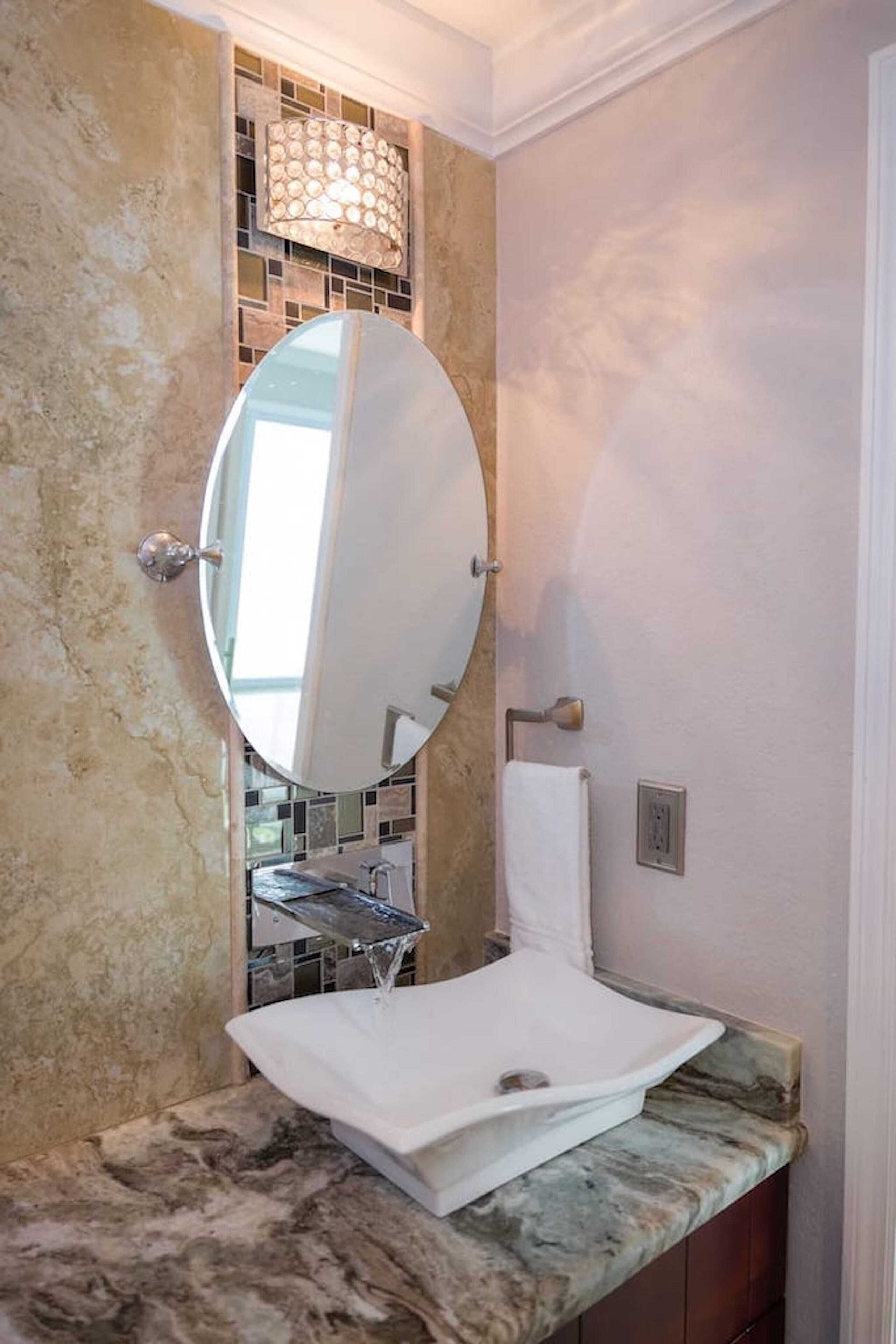 A bathroom with a marble sink, a large mirror, and a mosaic tile backsplash.
