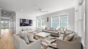 Ein geräumiges Wohnzimmer mit einem großen Flachbildfernseher, einer weißen Sofagarnitur, einem Couchtisch und einem gemusterten Teppich.