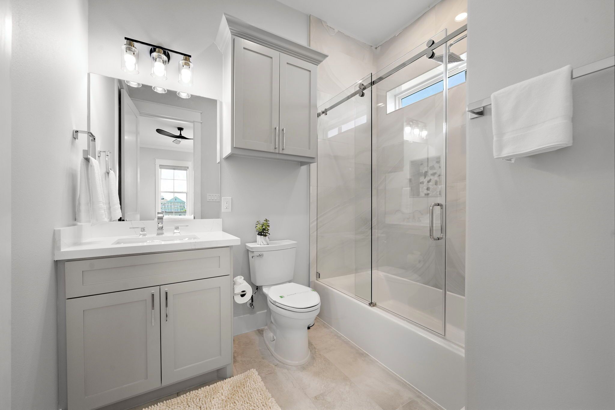 A modern bathroom with a glass-enclosed shower, a toilet, and a sink with a mirror above.