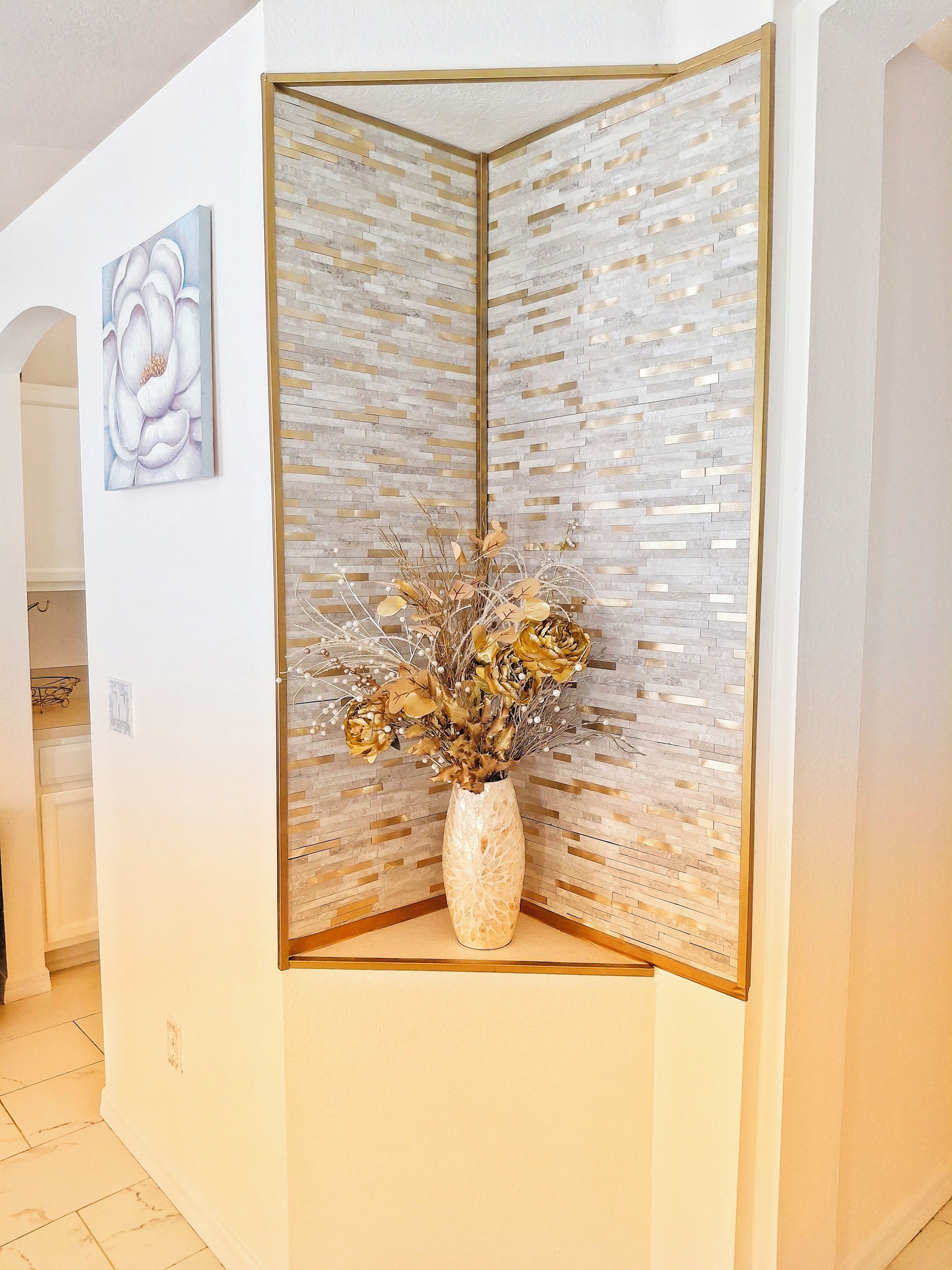 A room with a decorative mirror, a vase with dried flowers, and a framed artwork on the wall.