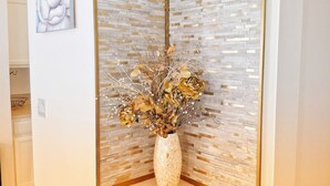 Una habitación con un espejo decorativo, un jarrón con flores secas y una obra de arte enmarcada en la pared.