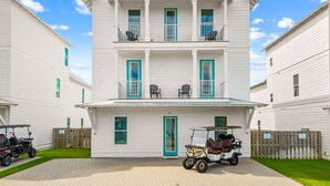 A two-story white building with a balcony on the second floor, a front door, and a driveway with two golf carts. - Ellis Retreat with LSV, Arcade, and Billiards (Miramar Beach)