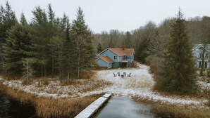 Ett hus med en brygga som sträcker sig ut i vattnet, omgivet av träd och snö.
