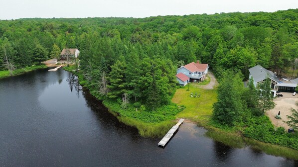 A lakeside property with a dock, a house with a red roof, and a large yard.