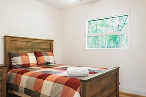 A bedroom with a wooden bed, a checkered bedspread, and a window with a view of trees.