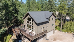 A two-story house with a deck, large windows, and a garage. - New! Hot tub, Fire Pit, Foosball Table! (Bigfork)