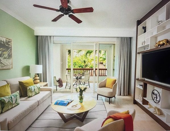 Una sala de estar con un sofá, sillones, una mesa de centro y un televisor. Hay un balcón con vista a zonas verdes.