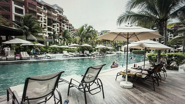 A hotel pool area with lounge chairs and umbrellas, surrounded by palm trees and a multi-story building. -  Available Dec 20-27th Christmas in the Sun 2bdrm 3 bath Luxury Condo In Cancun! (Cancún)