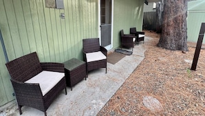 A covered outdoor seating area with wicker furniture and a door leading to the house.