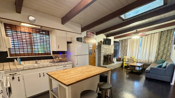 A kitchen with a wooden island, bar stools, and a dining area with a sofa and a table.