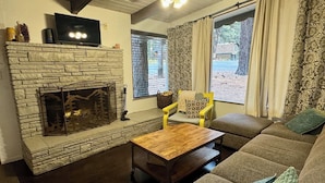 A cozy living room with a stone fireplace, a flat-screen TV, a sofa, and a coffee table.