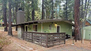 A rustic cabin with a stone foundation, a wooden fence, and a green exterior.