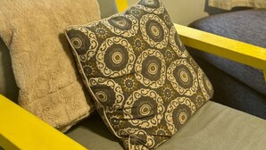 A room with a window view of a forested area, a yellow chair, and a sofa with patterned cushions.