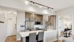 A modern kitchen with a central island, stainless steel appliances, and a dining area with bar stools. - Luxury 2 Bedroom Condo at The Mason Pool, Free Ski Shuttle, AC (Heber City)