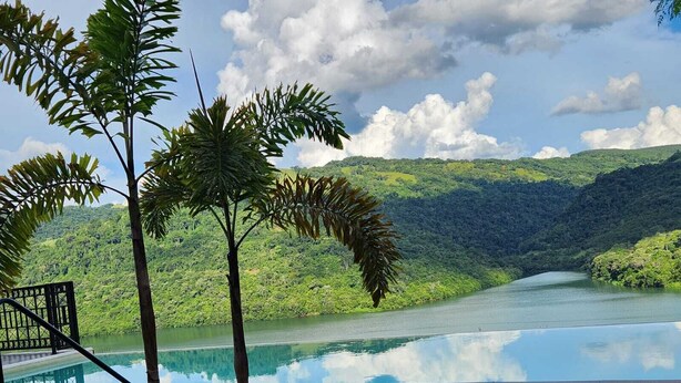 A wooden deck with a pool, surrounded by tropical plants and overlooking a calm lake with a mountainous backdrop. - Wonderful house with spectacular views of the Uruguay River - Goio En - Chapecó-SC (Chapecó)