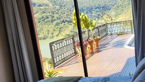 A bedroom with a large window overlooking a deck with a view of a lake and hills. - Wonderful house with spectacular views of the Uruguay River - Goio En - Chapecó-SC (Chapecó)