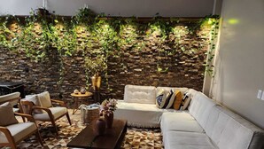 A cozy living area with a stone wall, a white sofa, wooden chairs, and a patterned floor. - Wonderful house with spectacular views of the Uruguay River - Goio En - Chapecó-SC (Chapecó)