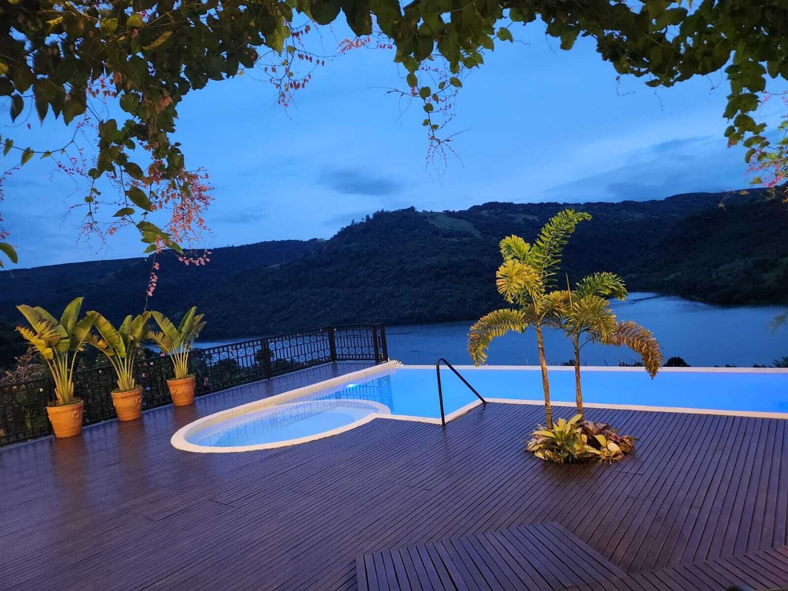 En træterrasse med swimmingpool, plantekasser og udsigt over en sø og bakker.
