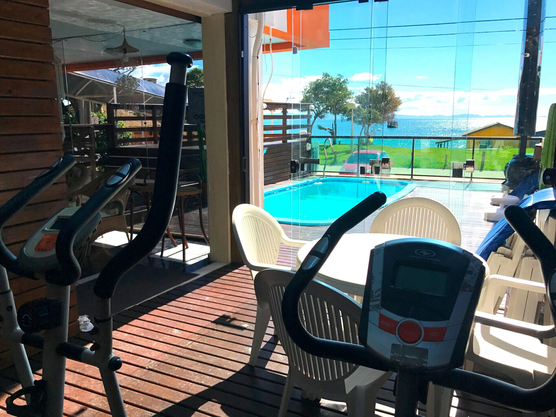 Uma área na piscina com equipamentos de ginástica, vista para o mar e um deck de madeira.