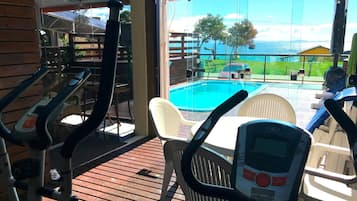 Uma área na piscina com equipamentos de ginástica, vista para o mar e um deck de madeira.