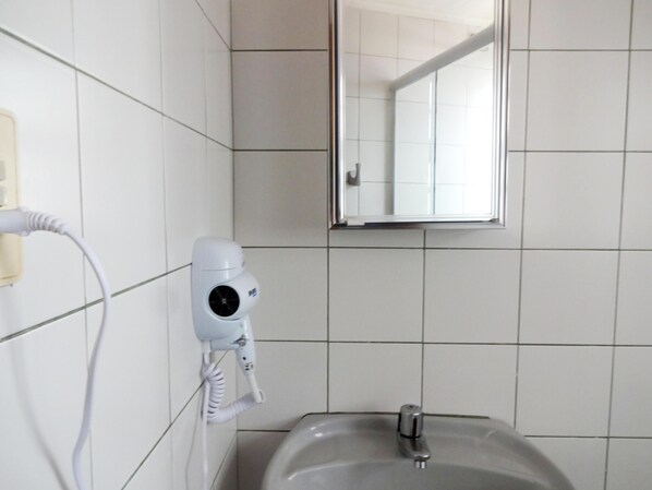 Une salle de bain avec un lavabo blanc, un miroir et un sèche-cheveux fixé au mur.