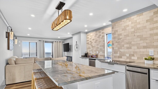 A modern kitchen with a marble island, white cabinetry, and a brick backsplash. - Oceanfront 3BR Dolphin Run condo with balcony and pool. (Virginia Beach)