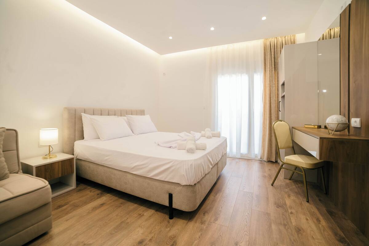 A modern hotel room with a large bed, a desk, a chair, and a wardrobe.