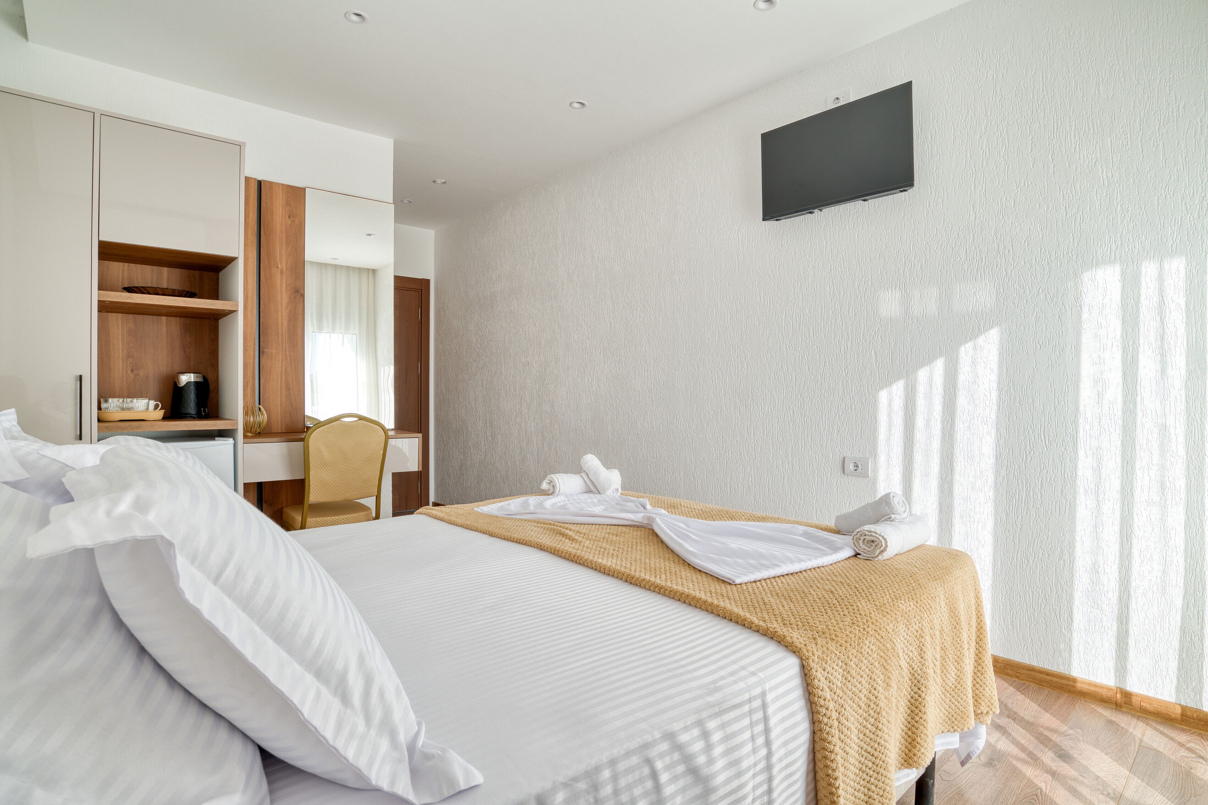 A hotel room with a bed, a TV mounted on the wall, and a wooden wardrobe.