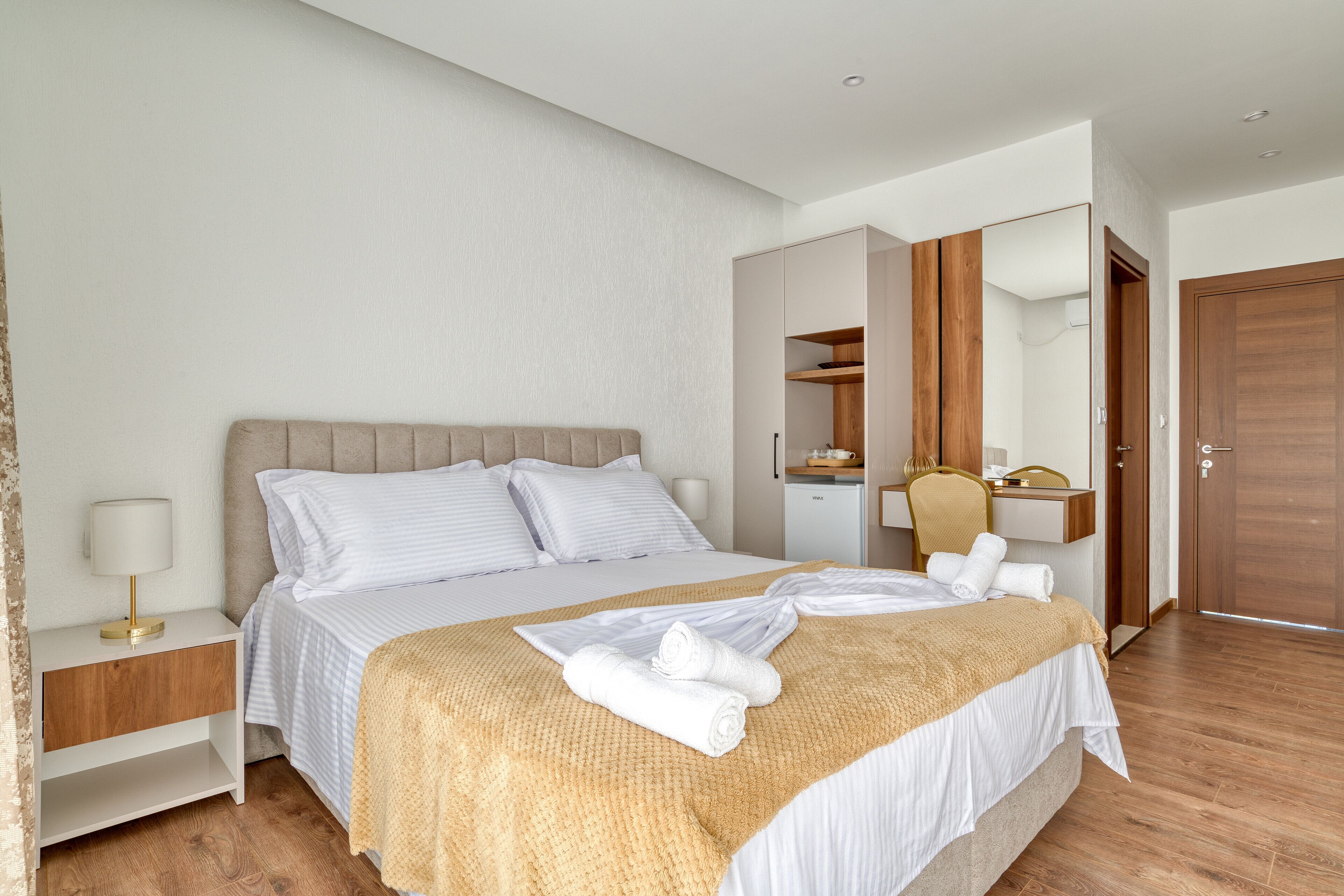 Ein ordentlich eingerichtetes Hotelzimmer mit einem großen Bett, einem Nachttisch mit Lampe, einem Kleiderschrank und einem Spiegel.