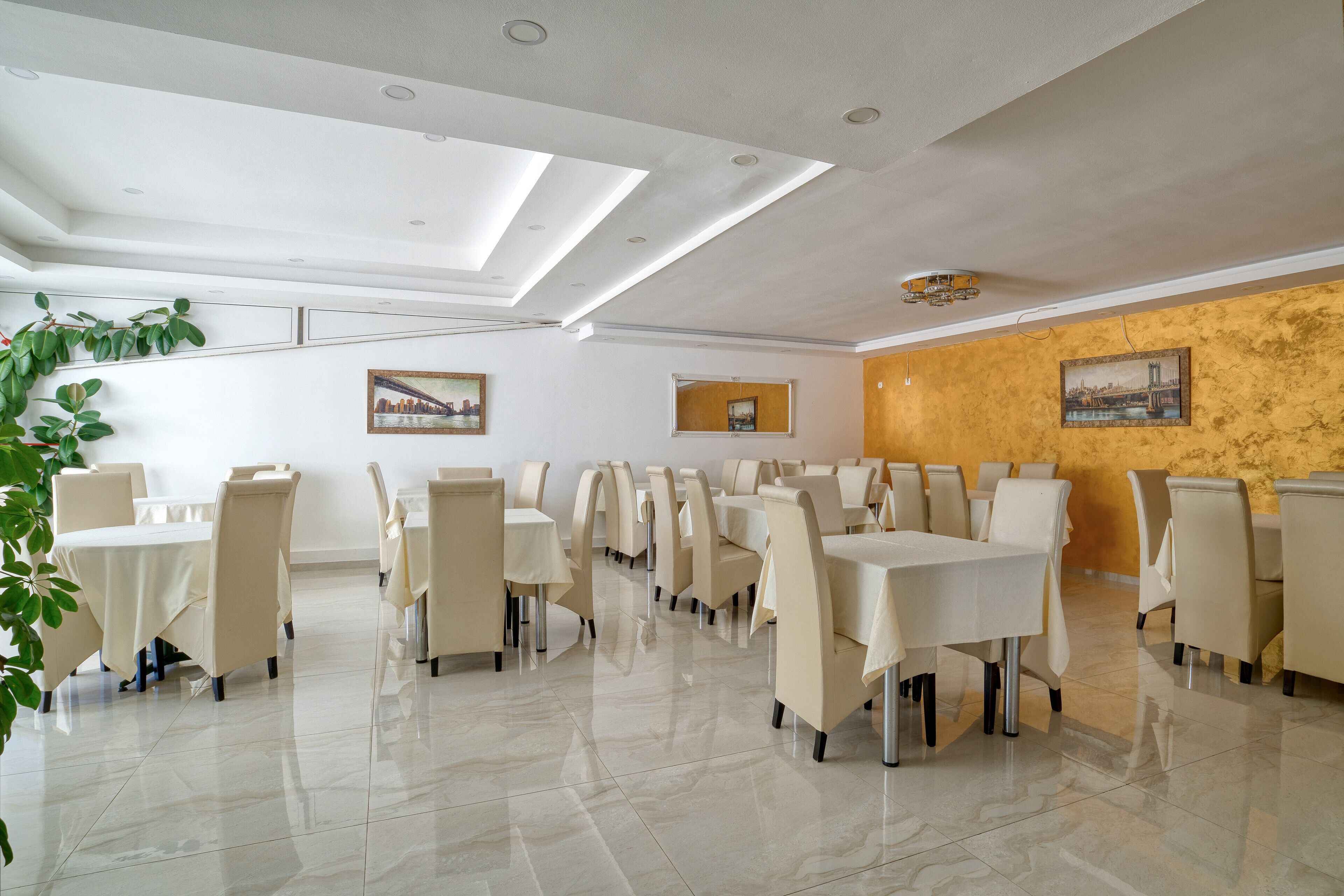 Un comedor amplio con varias mesas y sillas, un techo con tragaluces y una pared con un mural.