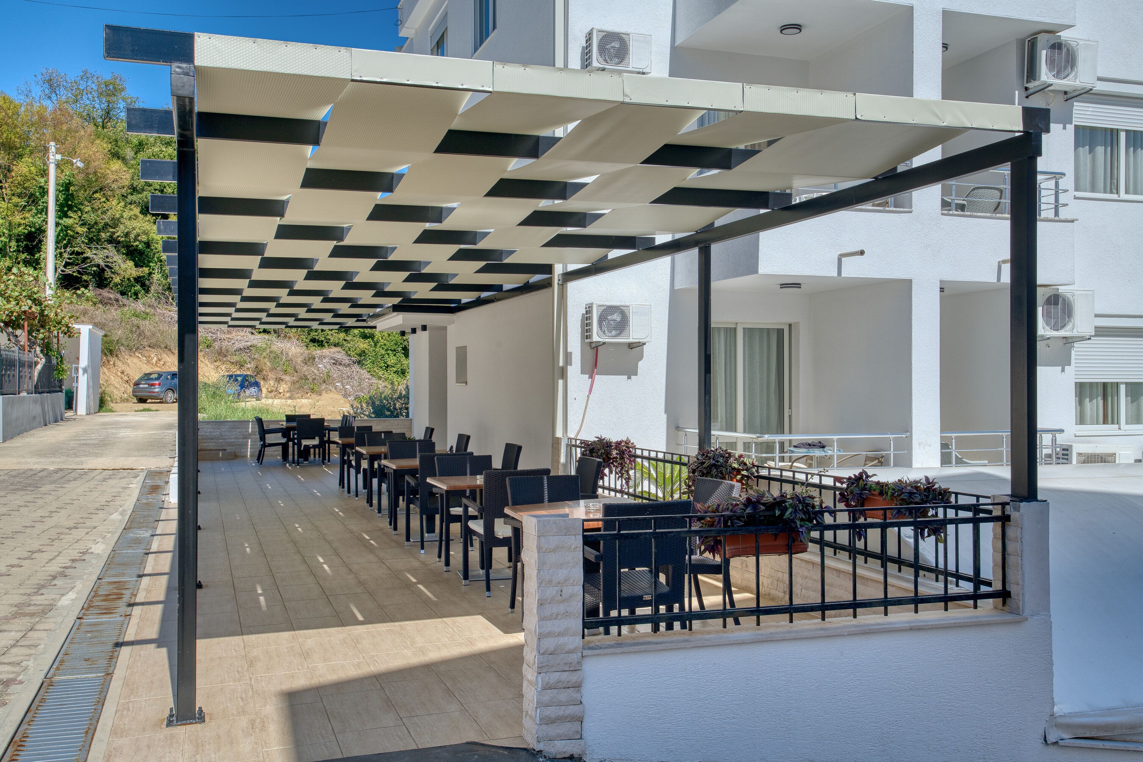 Un'area con posti a sedere all'aperto, tavoli e sedie, una pergola che offre ombra e condizionatori d'aria sulla facciata dell'edificio.
