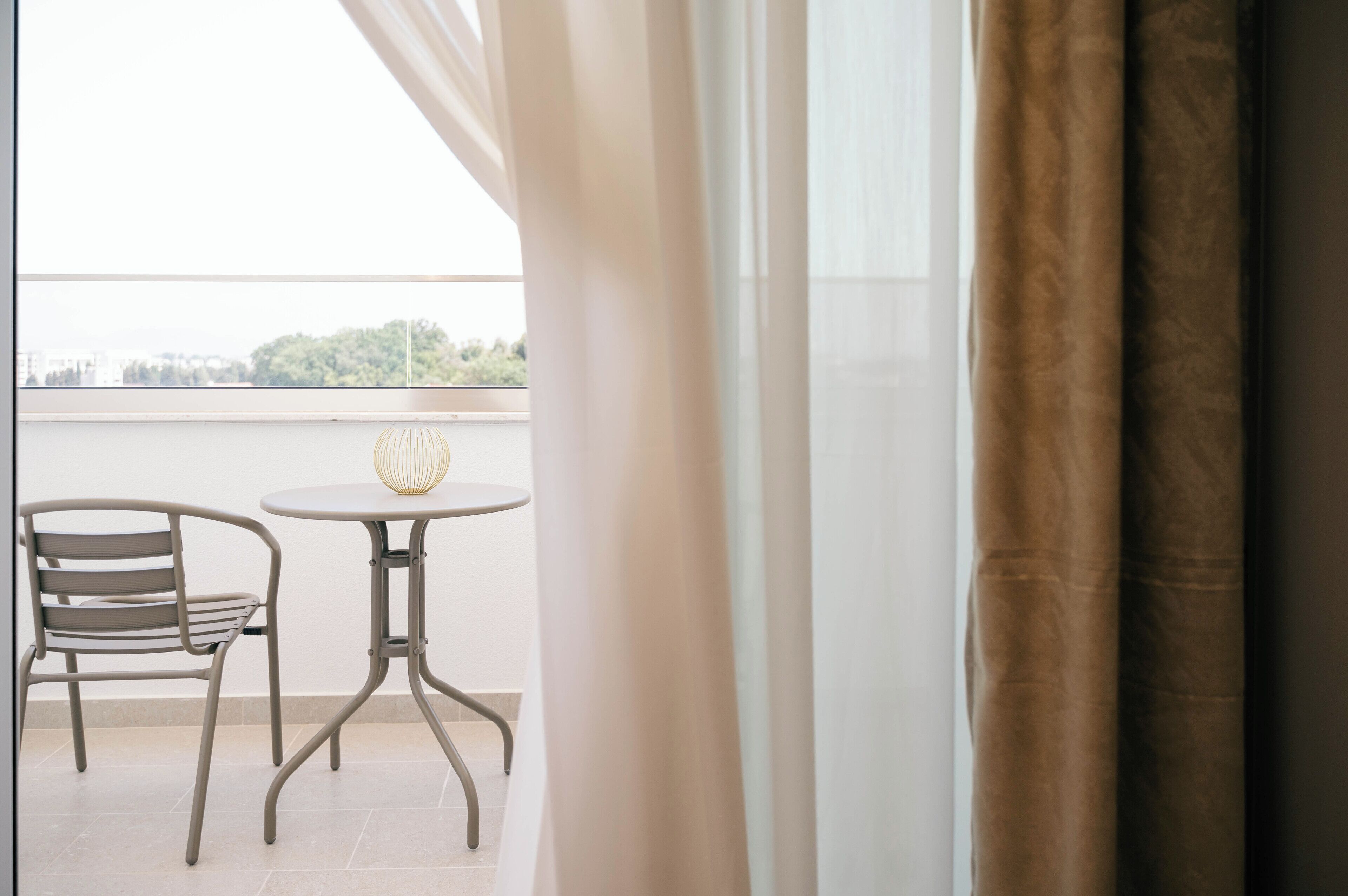 A balcony with a table and chair, a view of the city, and a curtain partially drawn.