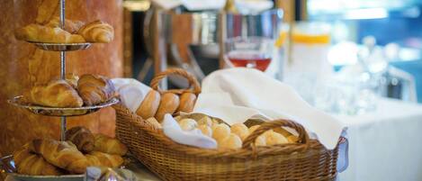 Una mesa de buffet con cruasanes y pan, una cesta de pan y una botella de champán al fondo.