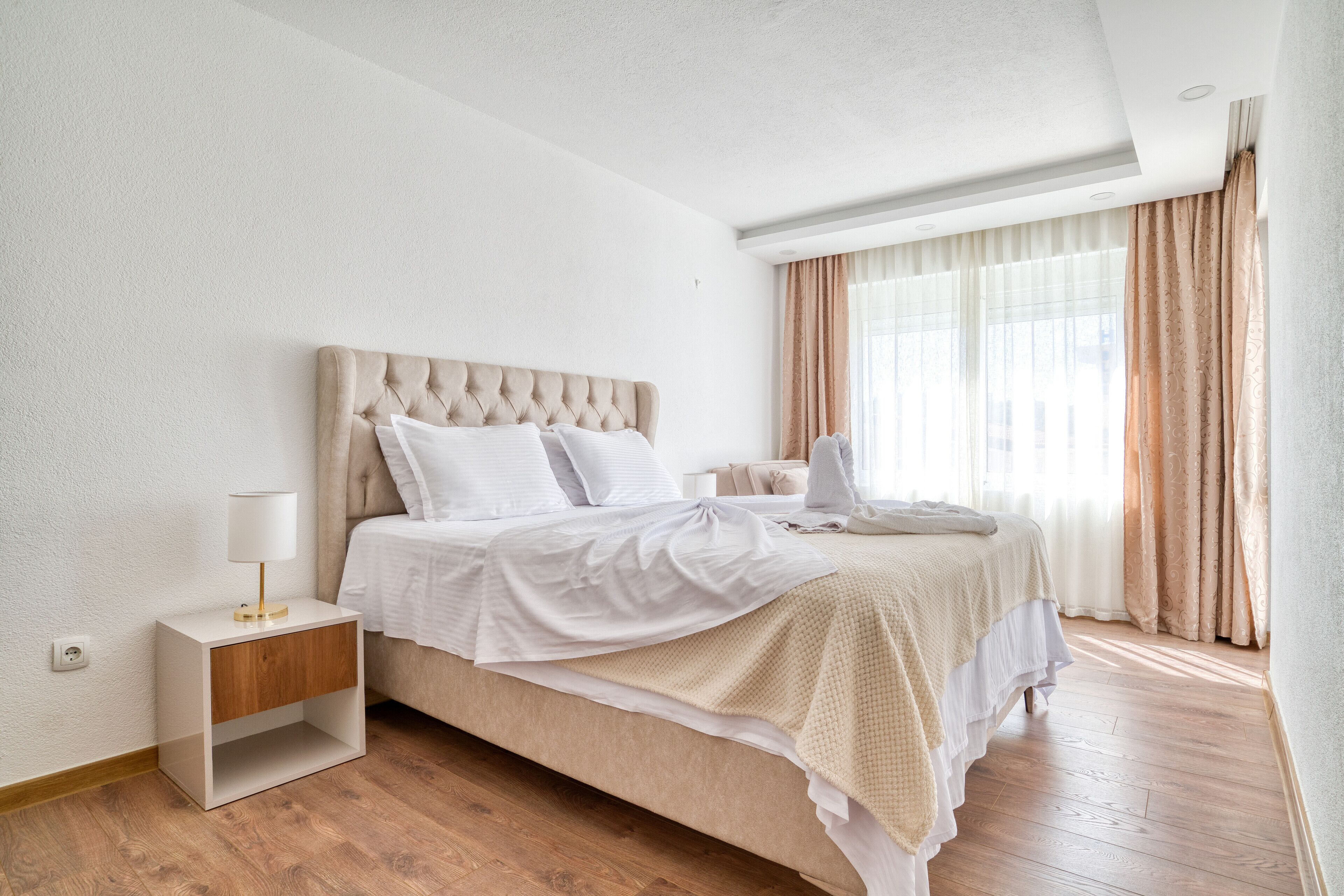 Quarto bem organizado com cama, mesa de cabeceira e janela com cortinas.