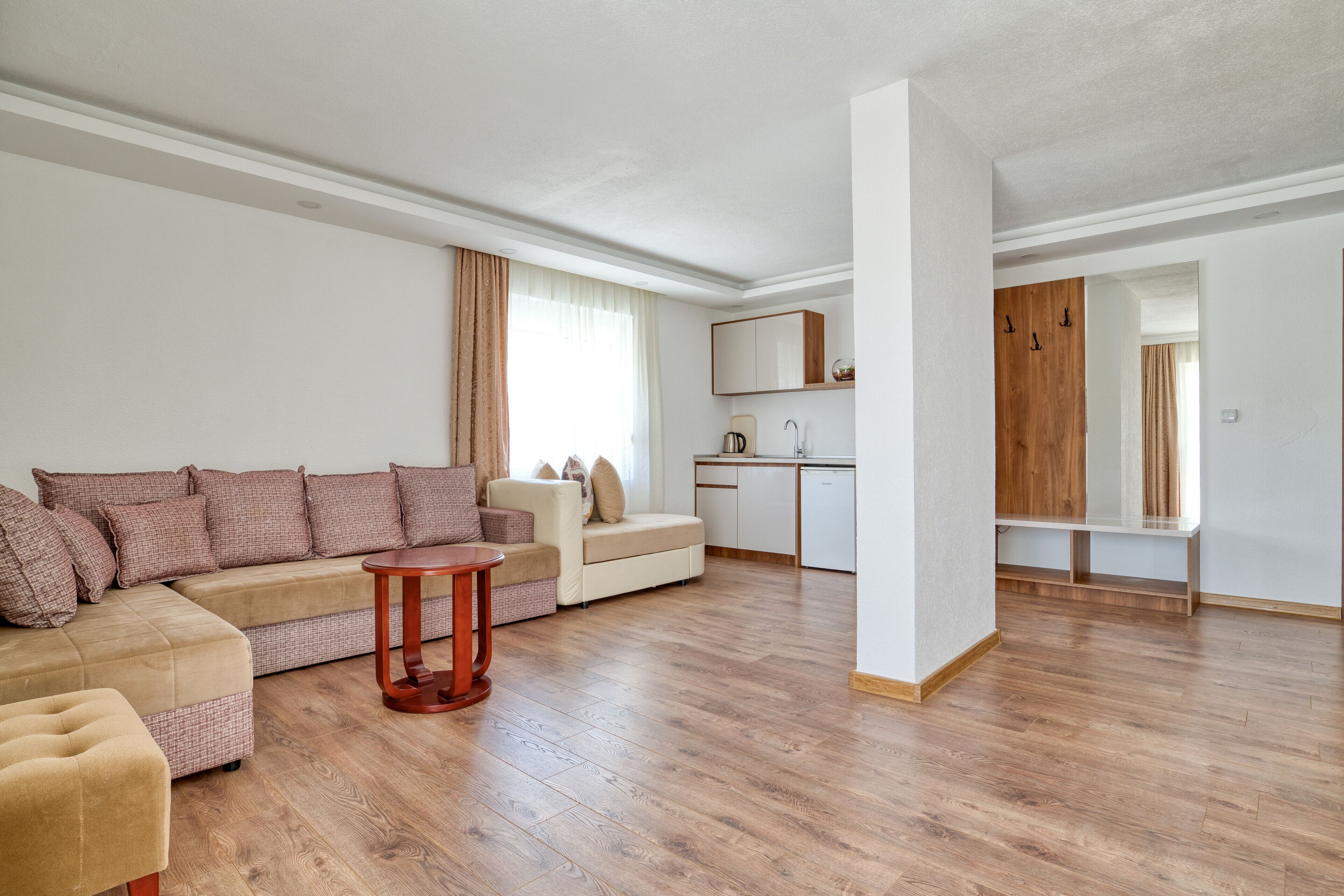 A modern living room with a beige sofa, a small round table, and a wooden floor.