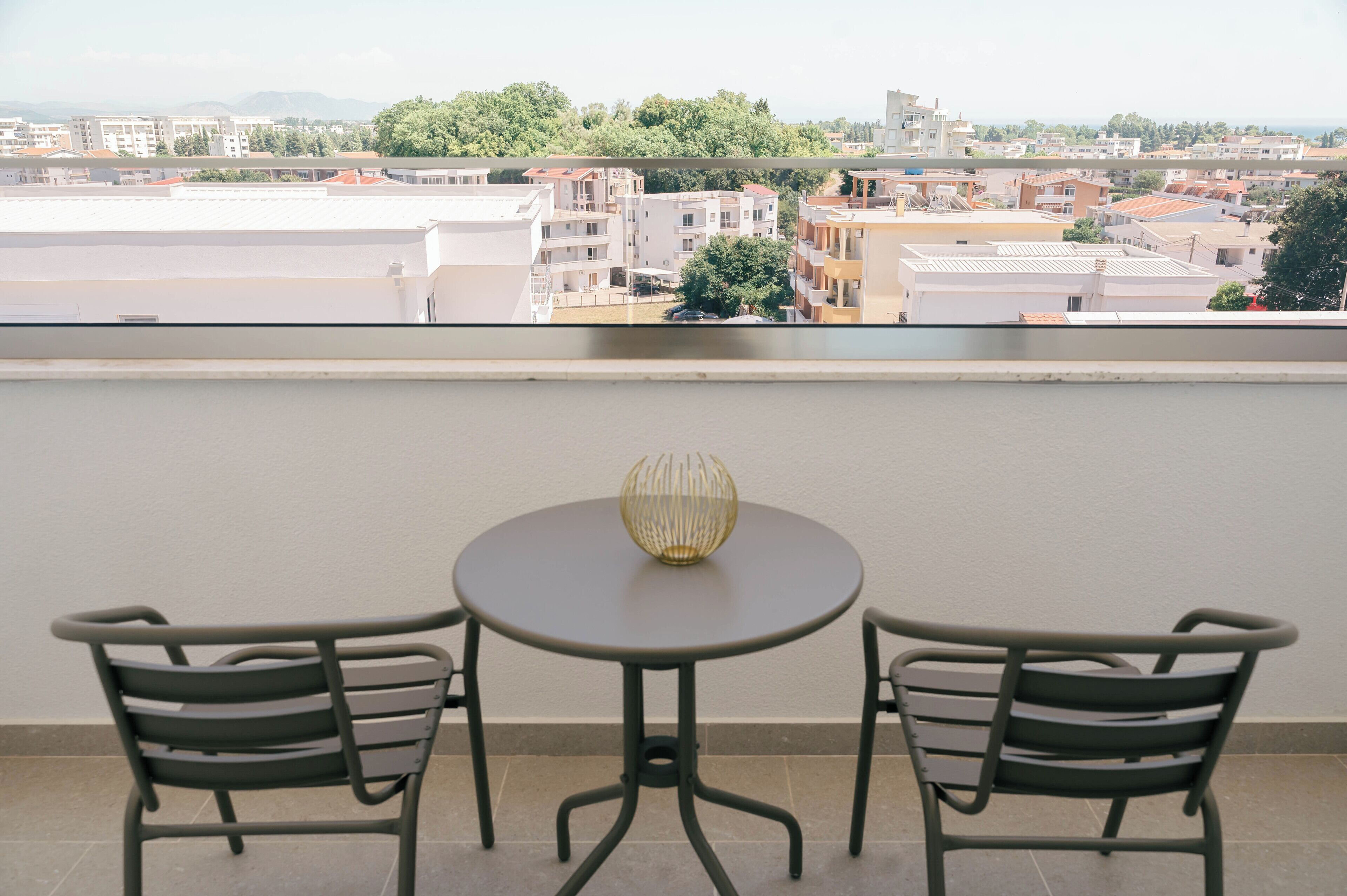 Un balcón con dos sillas y una mesa, con vistas a un paisaje urbano con edificios y árboles.