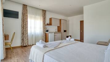 A modern hotel room with a large bed, a desk, a kitchenette, and a bathroom.
