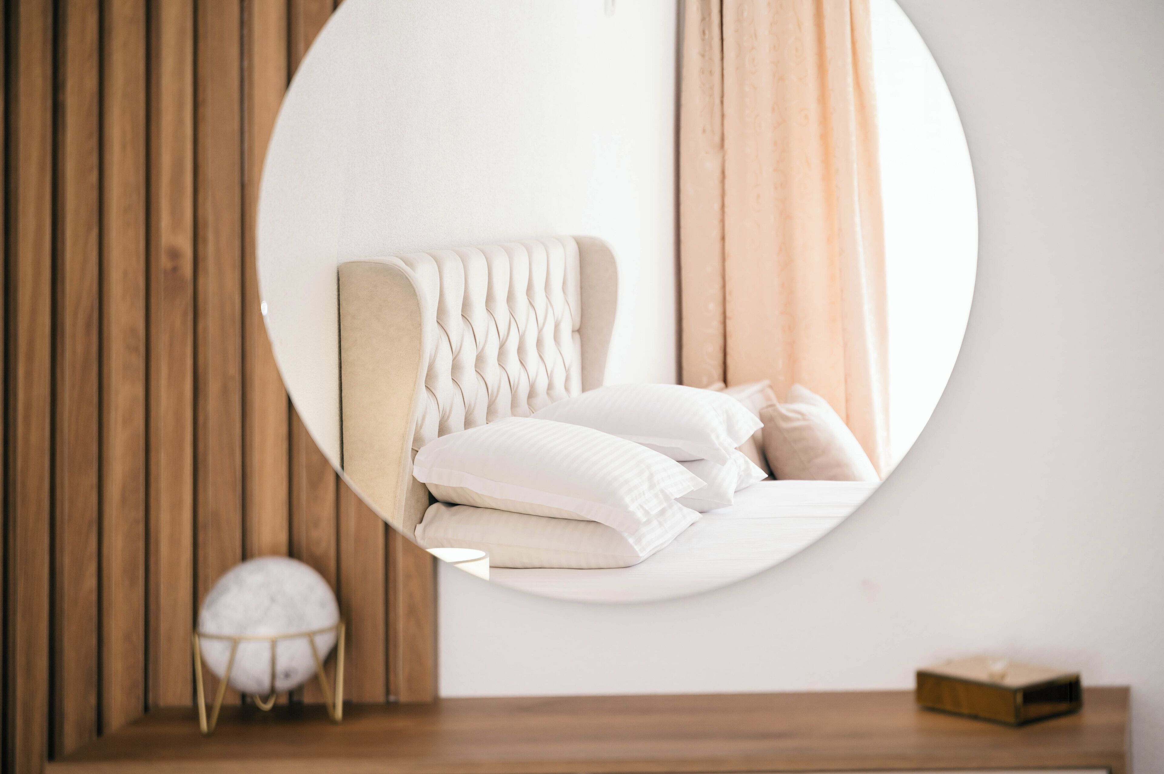 A bedroom with a round mirror reflecting a bed with white bedding and a wooden headboard.