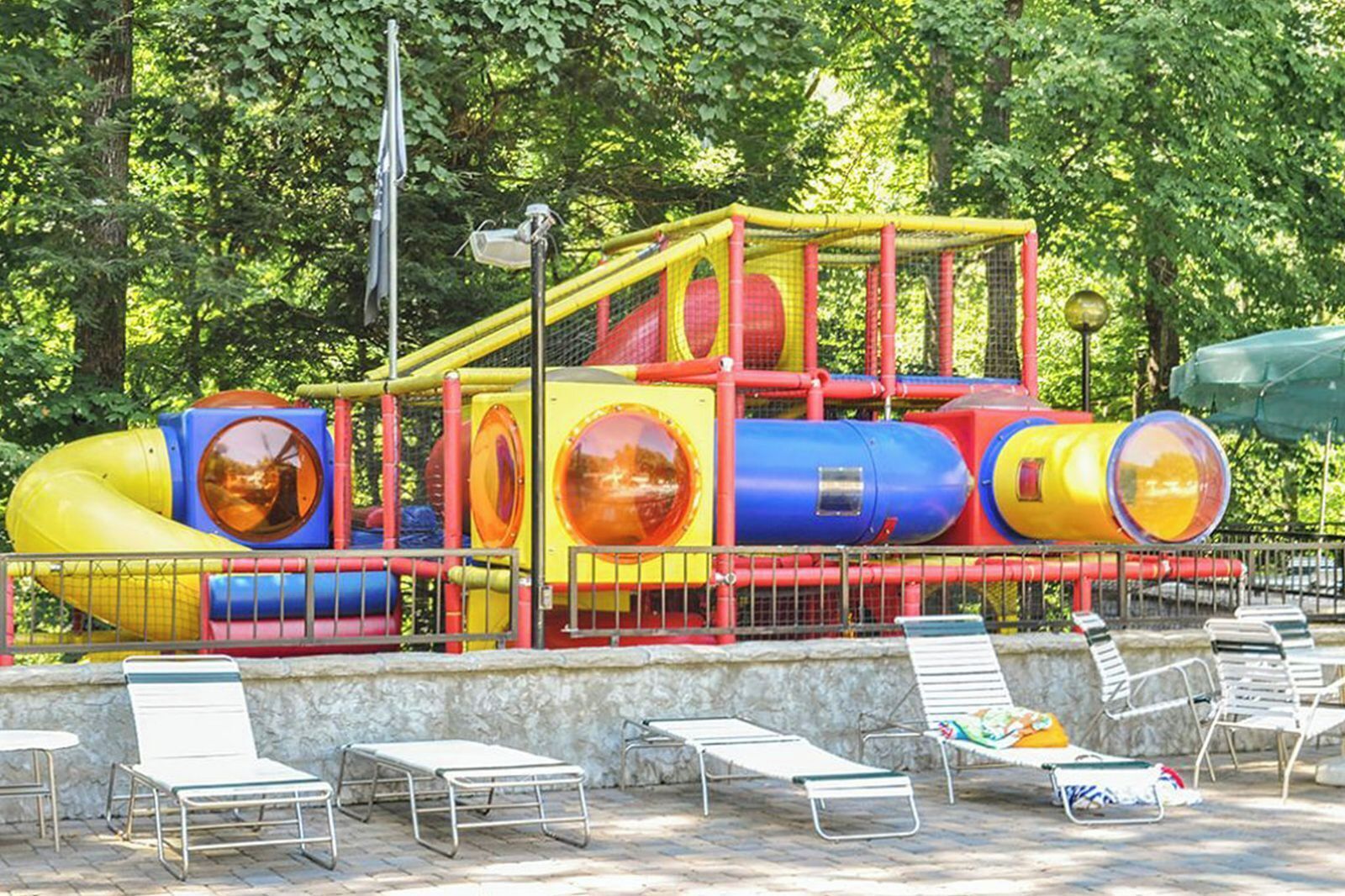 Ein Spielplatz mit Rutschen und Klettergerüsten, umgeben von Liegestühlen und einer Steinmauer.