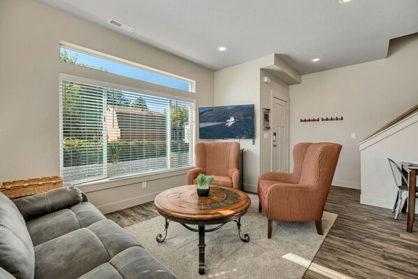 A living room with a gray sofa, two striped armchairs, a round coffee table with a plant, and a large window with blinds. - Hill Field 3 by CDH in Layton (Layton)
